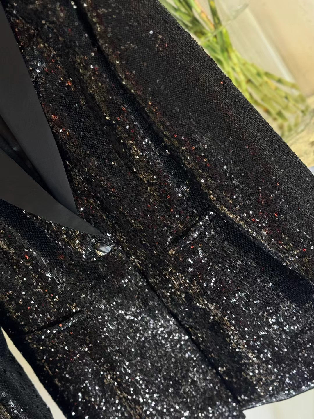 Close-up of black sequin fabric, smooth contrast lapel, and blazer button