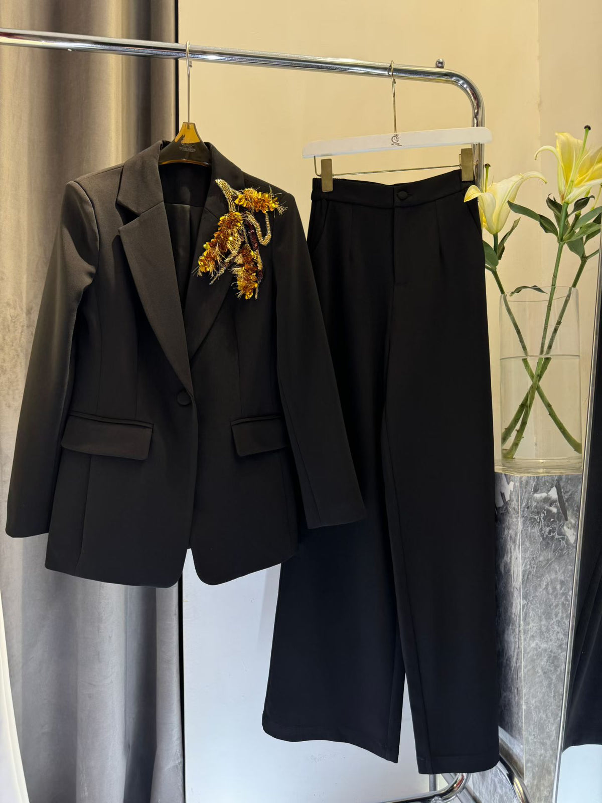 Black blazer and wide-leg pants on hangers with gold-tone shoulder appliqué